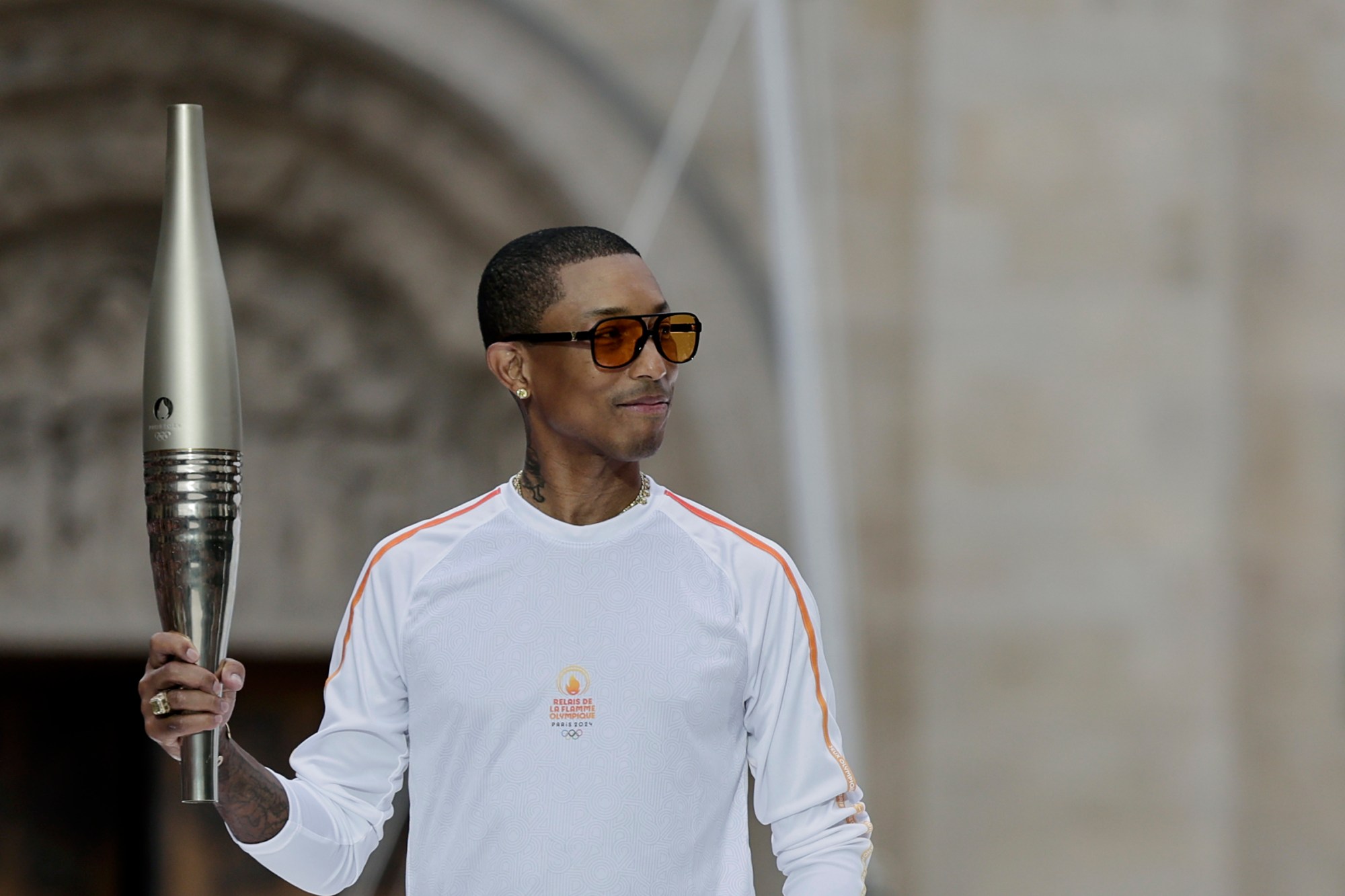 U.S. rapper, artist, and designer Pharell Williams holds the Olympic torch as part of the 2024 Summer Olympics torch relay ahead of the opening ceremony in Saint-Denis, outside Paris, Friday, July 26, 2024. (Stephane De Sakutin/Pool Photo via AP)